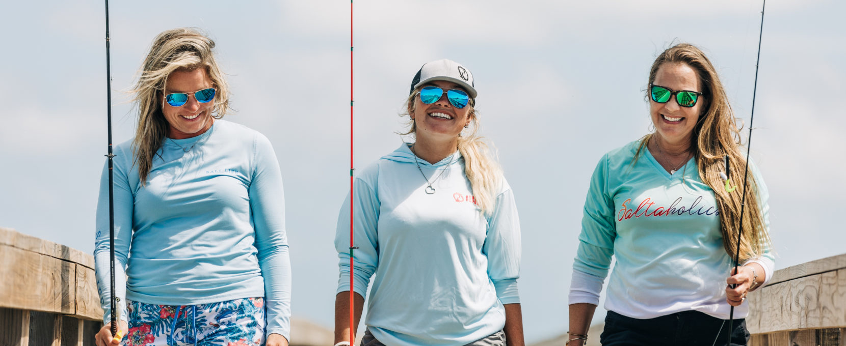 Three female anglers walking down fishing pier with gear in hand