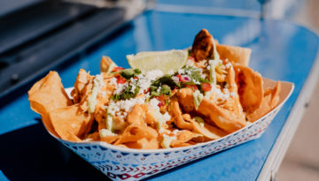 Serving tray of fresh nachos from Loli's Streatery, topped with enchilada sauce, queso fresco, cotija cheese cilantro, and pico de gallo.