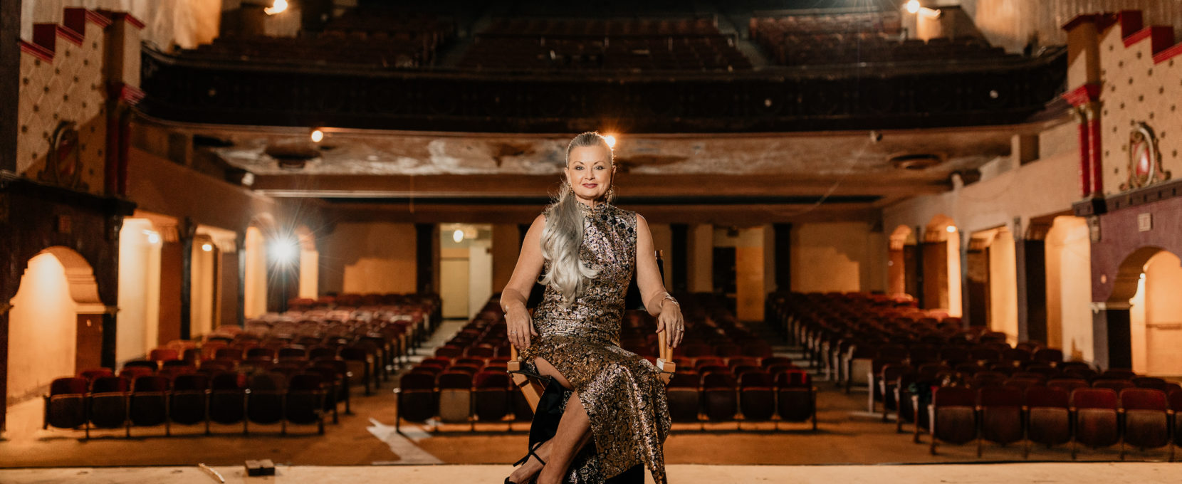 CCPATCH Executive Director, Cheryl Votzmeyer-Rios, sits in a director-style chair center stage in The Ritz Theatre.