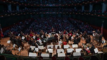The Corpus Christi Symphony Orchestra sits center-stage in the Performing Arts Center as the full crowd enjoys an orchestral performance.