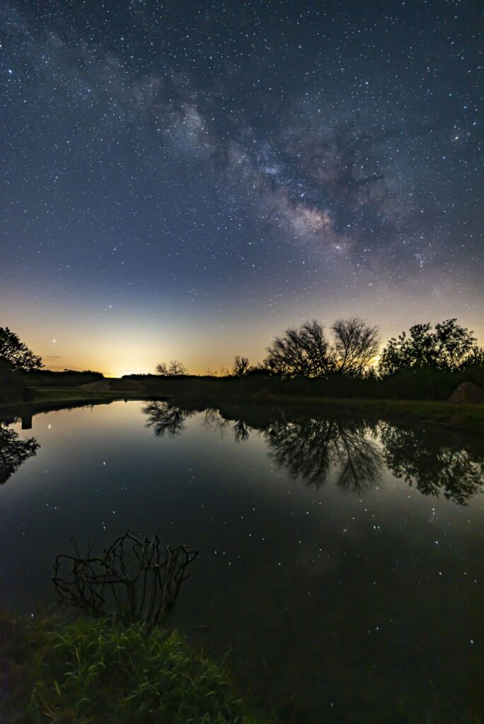 The stars of a clear night sky reflect on the still water of Phoinix Ranch, shot by Rey Garza and Jim Quisenberry, awarded 1st place in full frame.