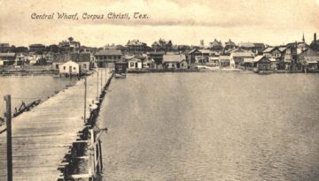 Corpus Christi History: A photo of Corpus Christi Wharf. Businesses line the coast, with the photographer standing on the end of the pier.