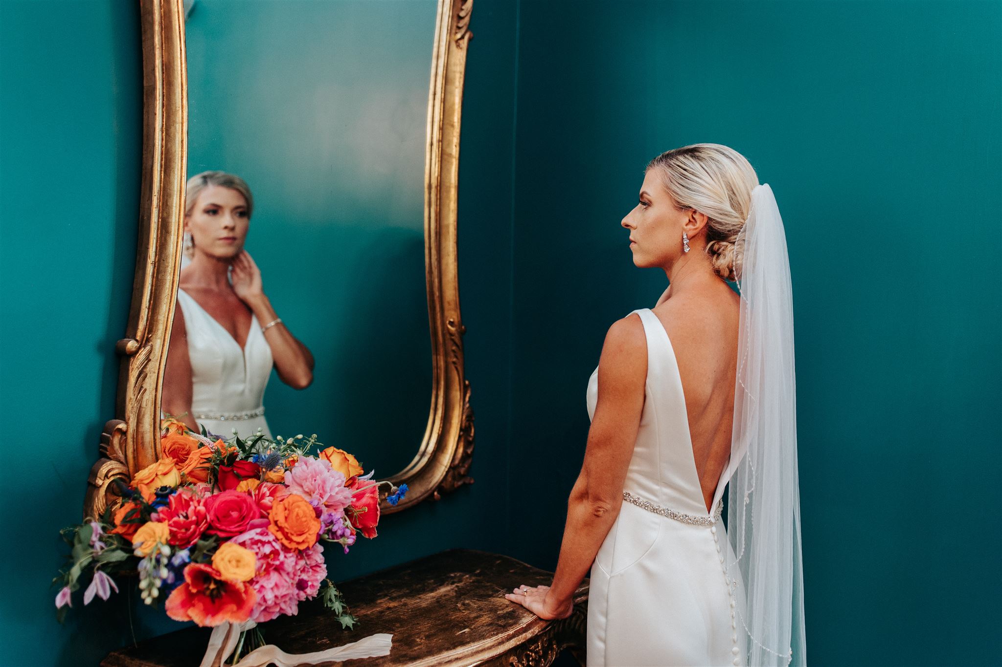 The bride looks into the mirror with vibrant florals, showcasing the bold jewel tones and vibrant florals of her summer wedding.