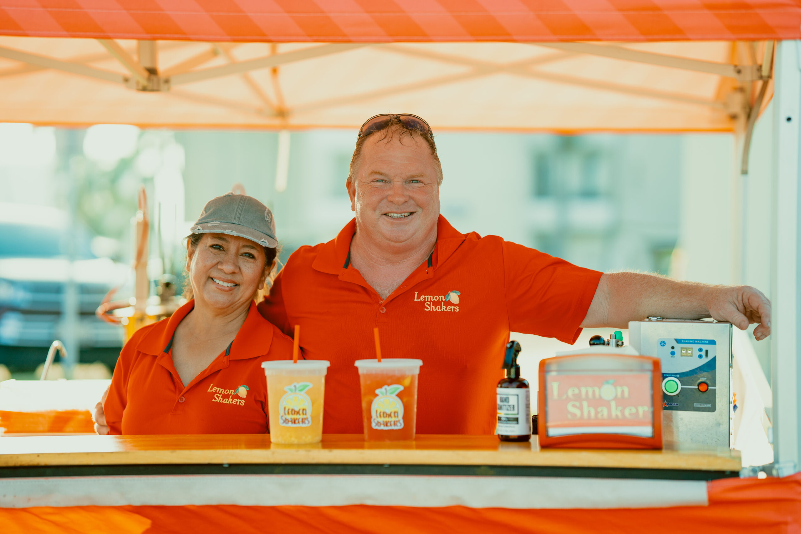Lemon Shakers owners, Sylvia and Marvin Kerr, stand joyfully in their pop-up lemonade stand behind fresh classic and strawberry lemonades.