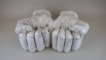 A photo of a plaster sculpture of two hands in upward facing fists sitting on a gray backdrop.