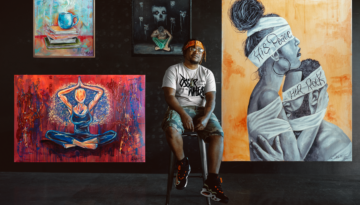 Corpus Christi artist Oscar "TrillJay" Wheat sits on a stool in front of a wall adorned with several of his paintings.