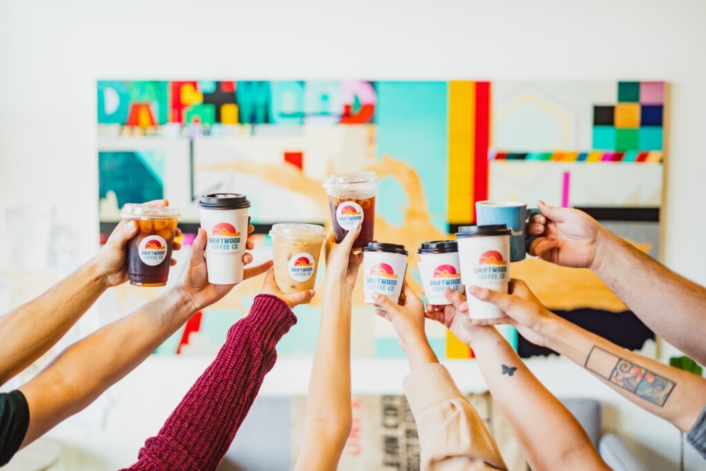 A group of hands holding up coffee cups from Driftwood Coffee Co. 