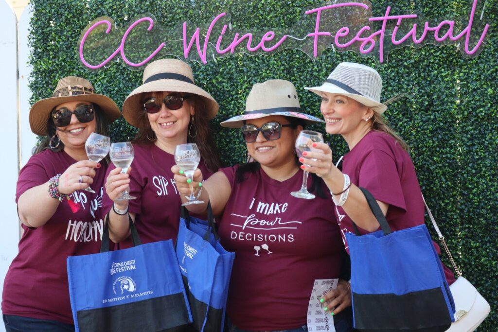 Four women posing with wine glasses at the Corpus Christi Wine Festival.