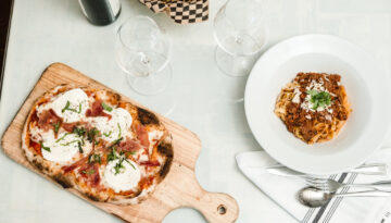A wine bottle and two glasses next to a pizza and pasta. Photo By Rachel Benavides