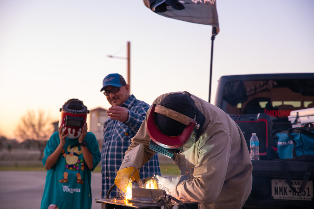 A student at Del Mar College demonstrates welding methods in front of a dad and his son.