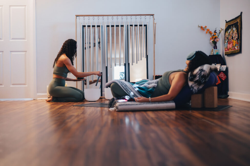 one woman meditating on the floor with her eyes closed, sitting down with tranquil music being played by the other woman. 