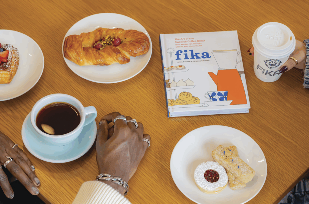 A table with pastries, coffee, a book, and two hands at Fika in Corpus Christi, Texas. 