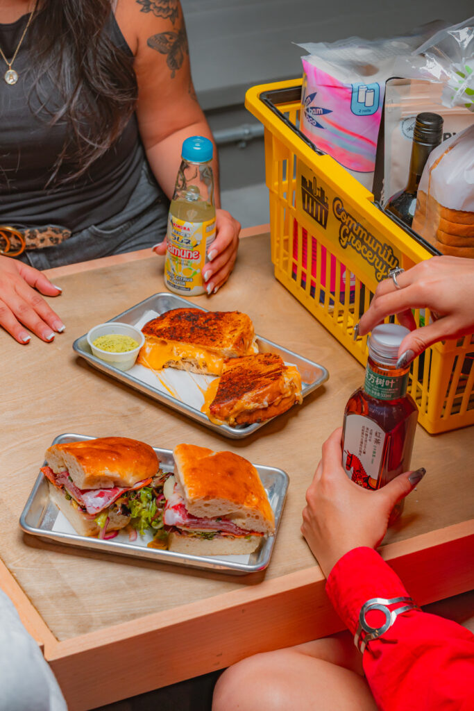 A table at Community Grocery in downtown Corpus Christi with sandwiches, drinks, and a shopping cart. 