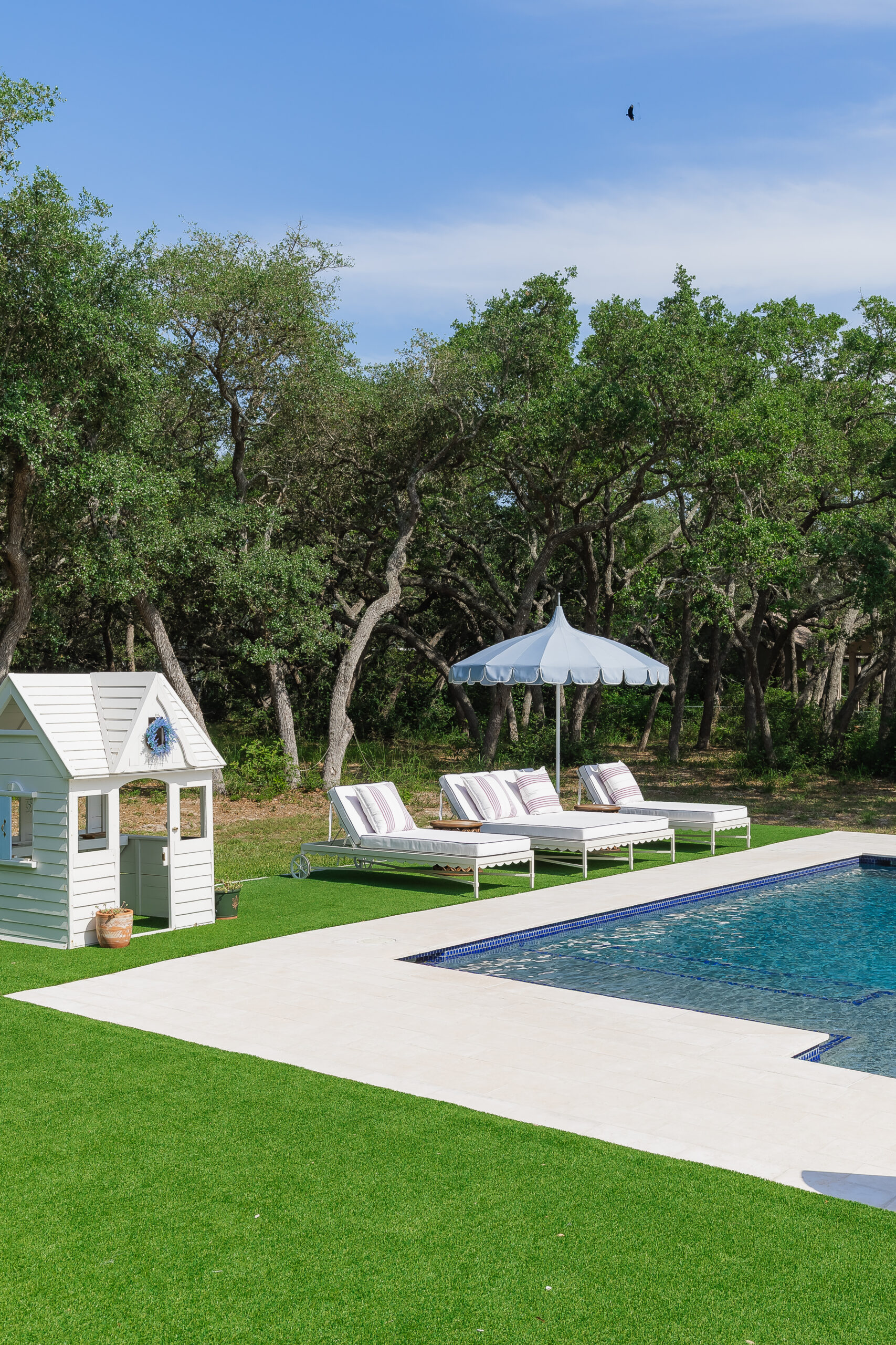 A resort-like experience, basking on chaises under scalloped canopies with the shimmer of a deep blue pool contrasting against the wild oak backdrop at a home in Rockport, Texas. 