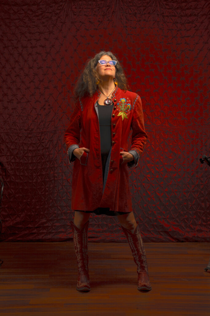 Stephanie Elizondo Griest stands in front of a red background with her face turned up toward to ceiling.