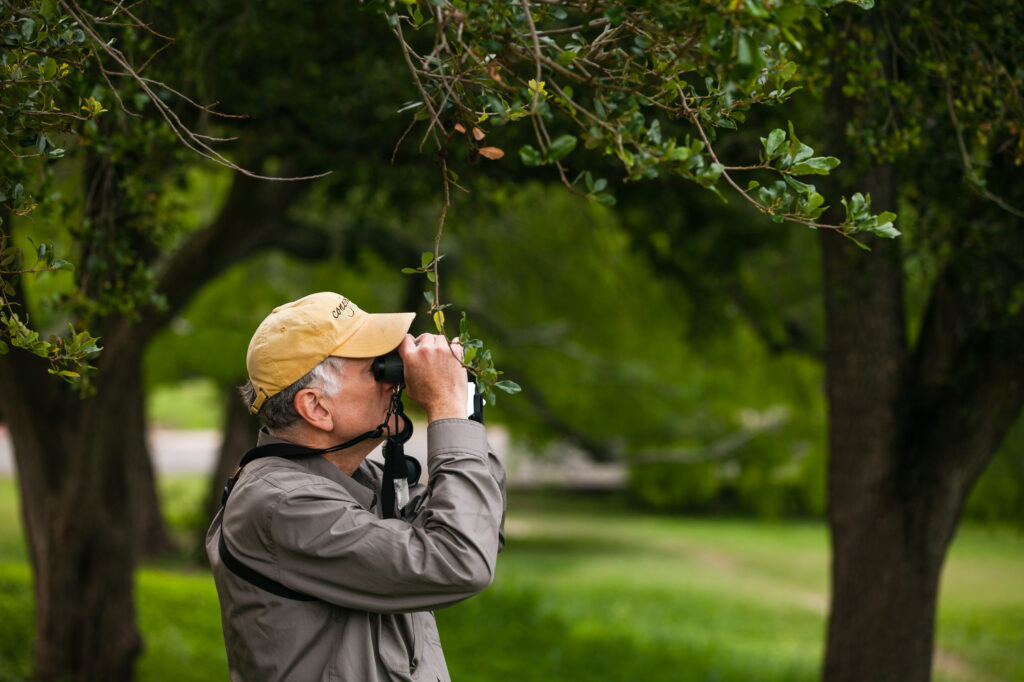 A man with binoculars in a forested area.