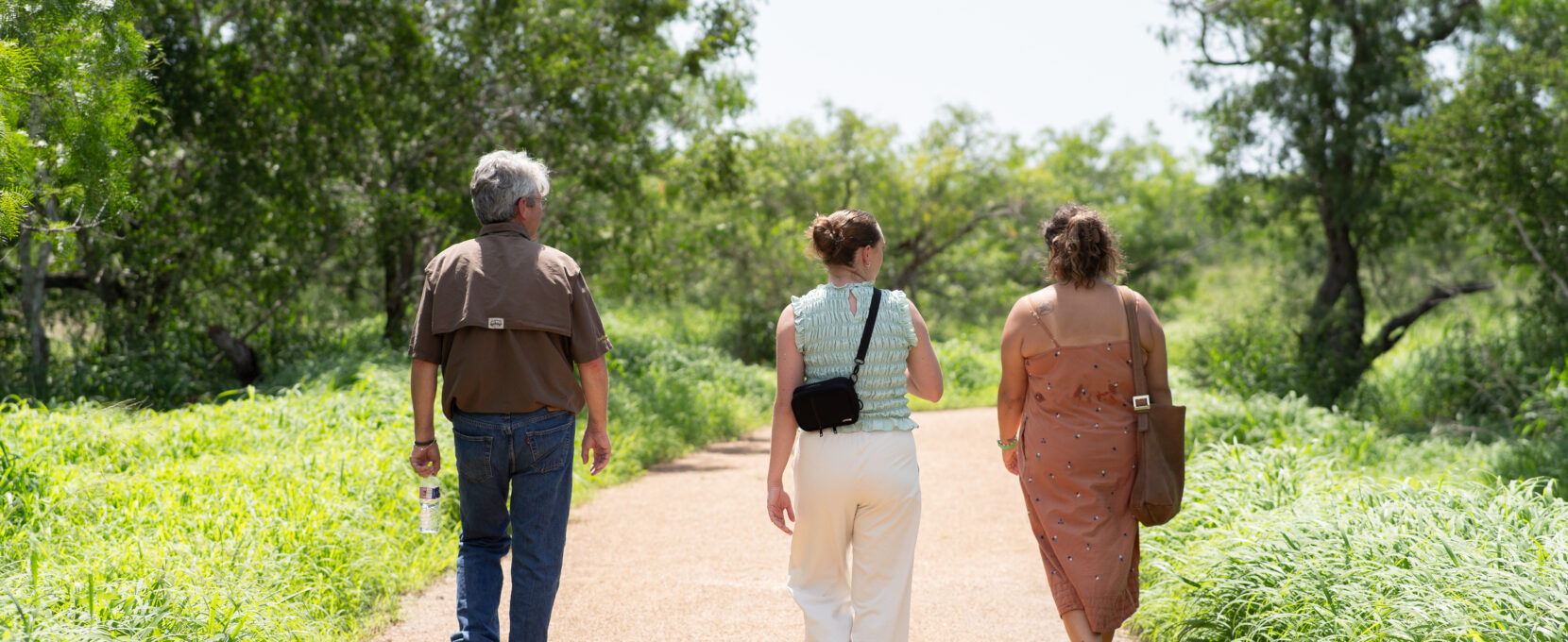Three adults walk down a paved trail.