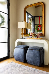 Two Santa Claus figurines on top of a white table with two velvet blue stools and a mirror greet guests in Stuart and Shannon White's home.