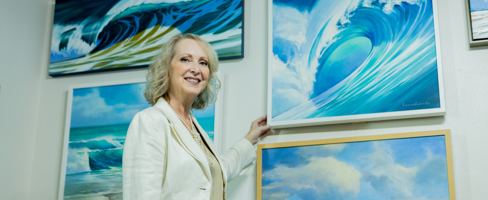 Artist Melissa Mitchell stands in front of her artwork of waves and oceans.