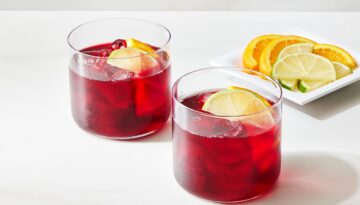 Two glasses of hibiscus tea with slices of lemon floating on top sit on a white countertop.