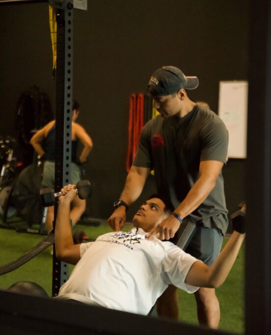 Personal trainer Alain Escobar helping a man lifting weights inside his gym AE Fitness.