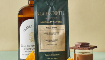 A bag of Kilate's Coffee's cold brew roast, a bottled version, and a glass styled with nuts, oranges, and chocolate.
