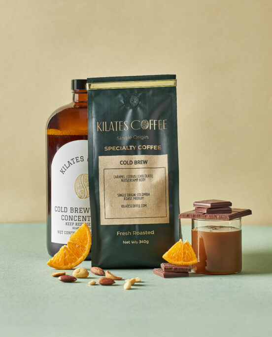 A bag of Kilate's Coffee's cold brew roast, a bottled version, and a glass styled with nuts, oranges, and chocolate.