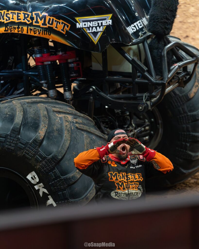 Monster truck driver Berto Treviño holds his hands up to his mouth in a yelling motion as he stands in front of his Monster Jam truck, Monster Mutt Rottweiler.