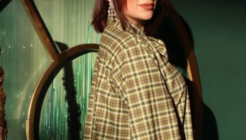 Clarissa Serna poses in front of a green background with a plaid outfit on.