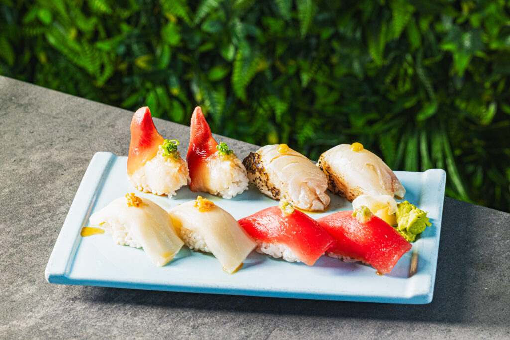 The photo features a spread of seafood on a turquoise platter. The platter sits on a dark stone set against a green, leafy background.