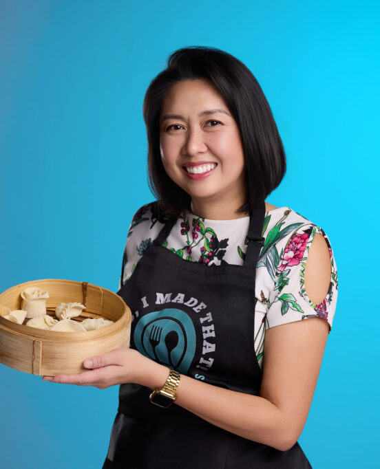 Noemi Medrano, aka Mimi Kitchenboss, poses with dumplings in front of a blue background.