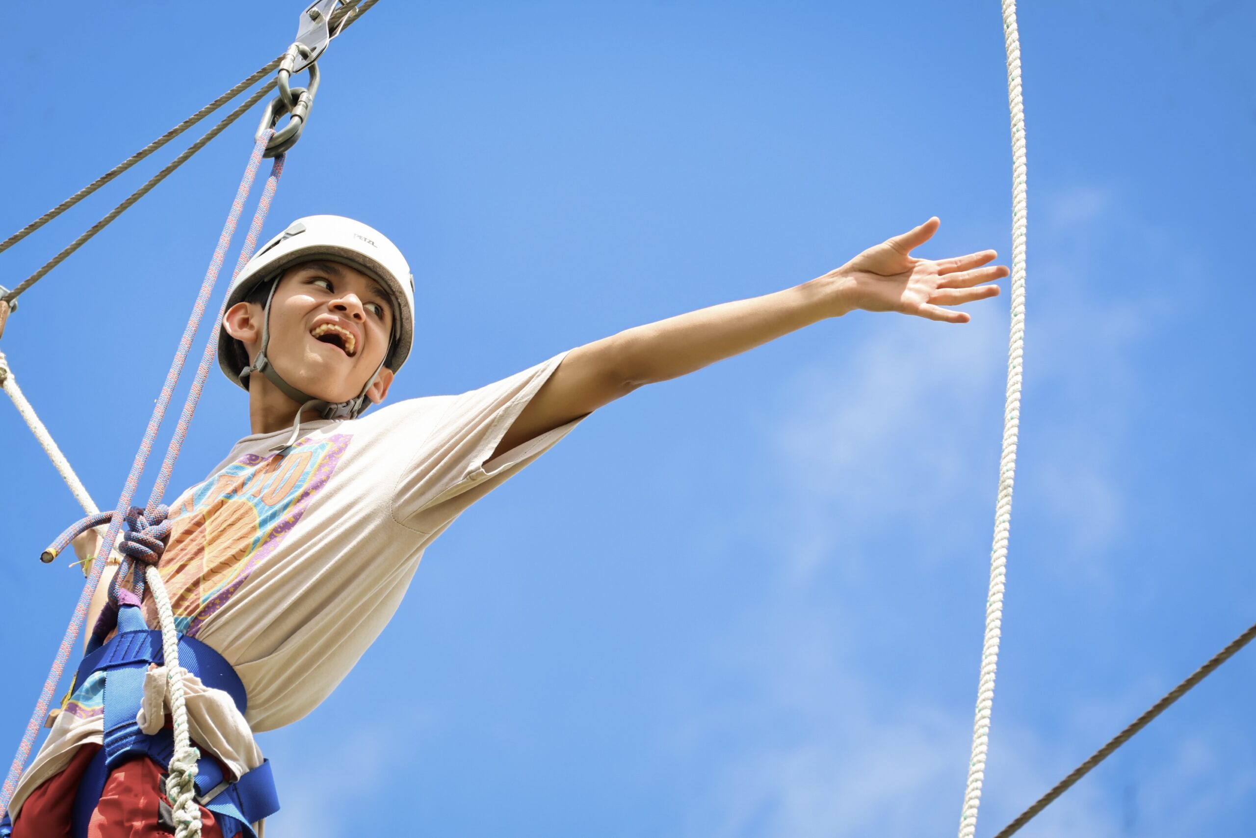 A boy hangs in a harness, reaching for a swinging rope, at Camp Aranzazu.