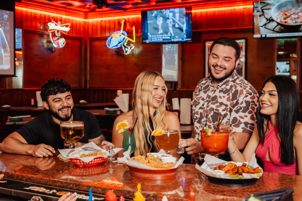 Two men and two women laughing over food and drinks at Wings N More Restaurant & Bar.