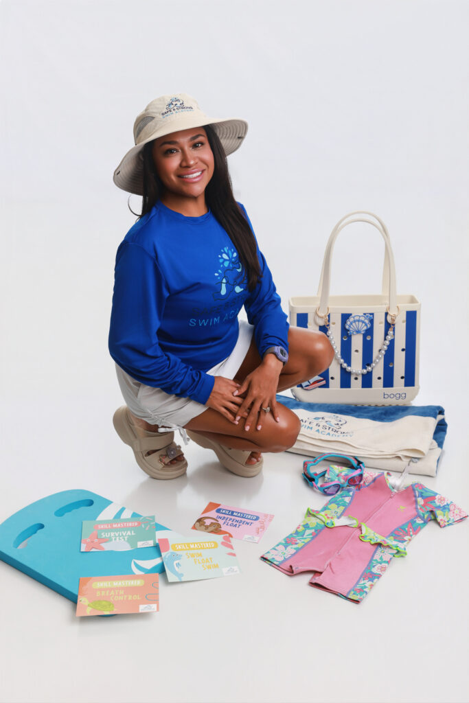 Head of Safe and Strong Swim, Yvette Segovia, crouches in a pose. She is surrounded by the business's merchandise and a white background.