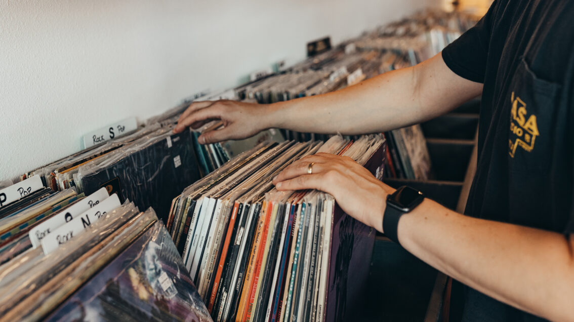 An individual flips through vinyl records on a shelf at Hybrid Records in Corpus Christi, Texas.