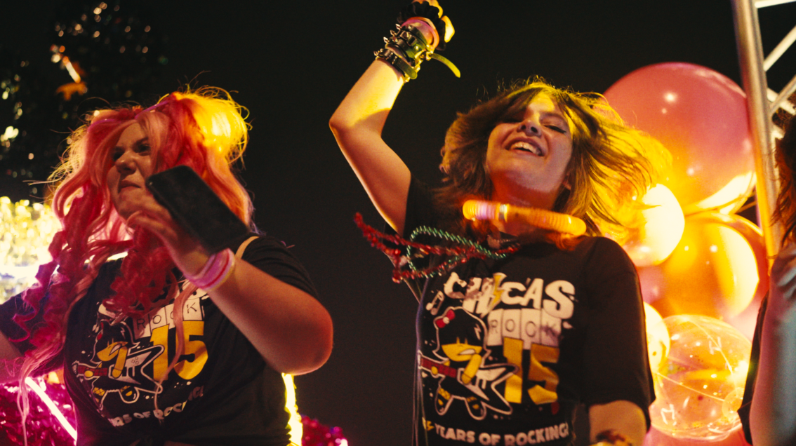 Two young girls are seen dancing on stage in Chicas Rock shirts.
