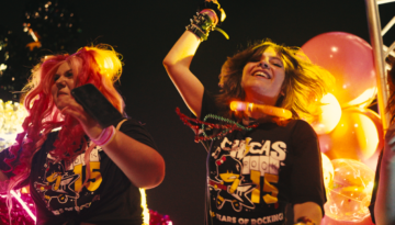 Two young girls are seen dancing on stage in Chicas Rock shirts.