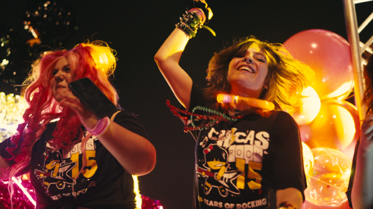 Two young girls are seen dancing on stage in Chicas Rock shirts.